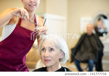 Cropped young woman master completes creation of senior female clients image with help of scissors Cropped young woman master completes creation of senior female clients image with help of scissors 141777716