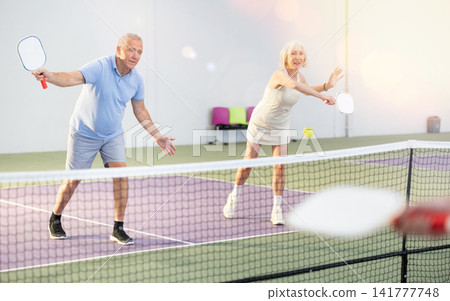 Couple of senior woman and man playing doubles pickleball indoors Couple of senior woman and man playing doubles pickleball indoors 141777748