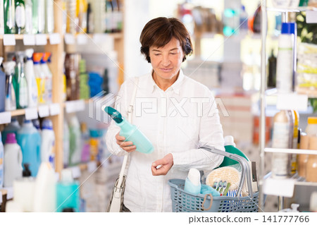 Woman selects various household cleaning products for cleaning the house with full basket of various purchases Woman selects various household cleaning products for cleaning the house with full basket of various purchases 141777766