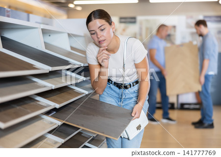 Young woman carefully examine flooring wood material laminate Young woman carefully examine flooring wood material laminate 141777769