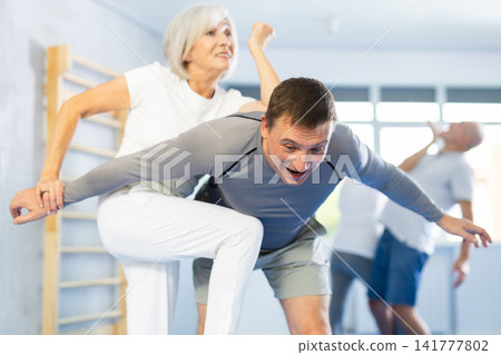 Senior woman in pair with middle-aged coach train Krav Maga and self-defense skills. Senior woman in pair with middle-aged coach train Krav Maga and self-defense skills. 141777802
