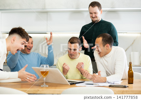 Group of friends watching football match on a laptop together and drinking beer Group of friends watching football match on a laptop together and drinking beer 141777858