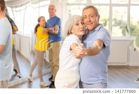 Group of elderly pensioners learn to dance a couple tango dance in dance class Group of elderly pensioners learn to dance a couple tango dance in dance class 141777860