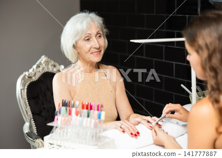 Smiling elderly woman receiving manicure from female manicurist in salon Smiling elderly woman receiving manicure from female manicurist in salon 141777887
