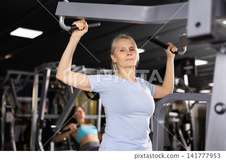 Mature woman pulls his arms to his chest on special simulator Mature woman pulls his arms to his chest on special simulator 141777953
