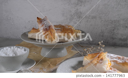 Crispy Baked Pastries Dusted with Powdered Sugar on a Gray Ceramic Cake Stand Crispy Baked Pastries Dusted with Powdered Sugar on a Gray Ceramic Cake Stand 141777963