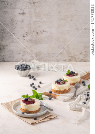 Mini cheesecakes with blueberry topping and mint leaves on a white rustic surface Mini cheesecakes with blueberry topping and mint leaves on a white rustic surface 141778038
