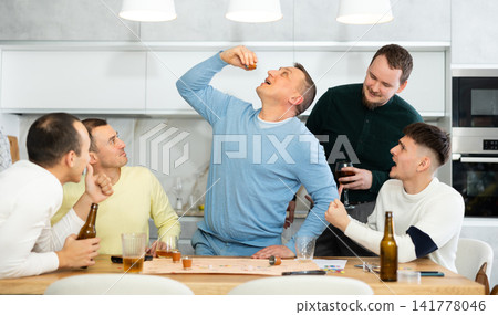 Group of friends excitedly playing board games and drinking beer at home Group of friends excitedly playing board games and drinking beer at home 141778046