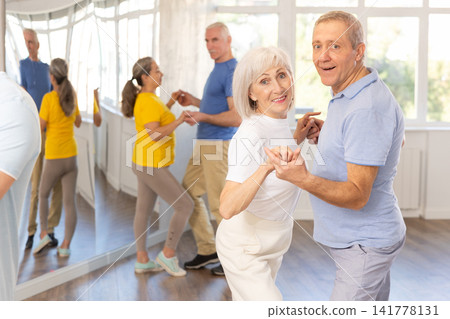 Group of happy mature pensioners learning to dance latin dances in dance studio Group of happy mature pensioners learning to dance latin dances in dance studio 141778131