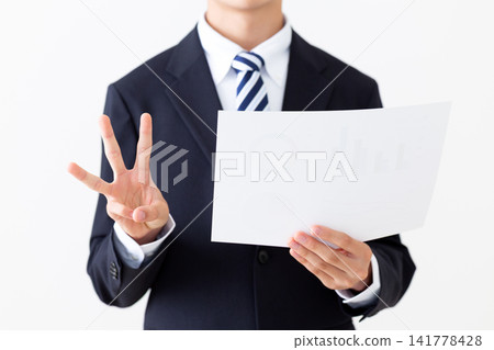 A young businessman in a suit holds up three fingers while looking at a graph. A young businessman in a suit holds up three fingers while looking at a graph. 141778428