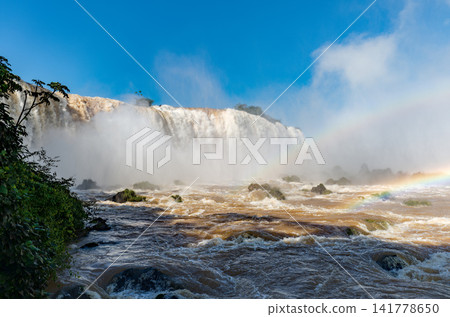 The majestic Iguazu Falls and the raging torrent of rocks emerge from behind a thick mist. The majestic Iguazu Falls and the raging torrent of rocks emerge from behind a thick mist. 141778650