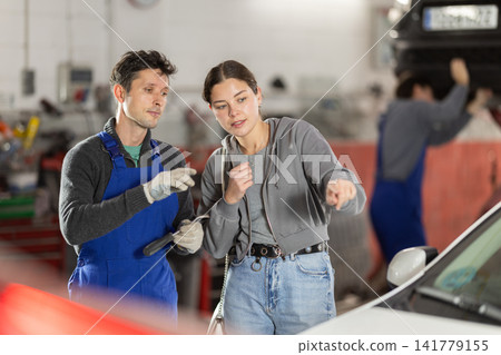 Male auto mechanic discussing with woman the cost and time to repair her car at car service Male auto mechanic discussing with woman the cost and time to repair her car at car service 141779155