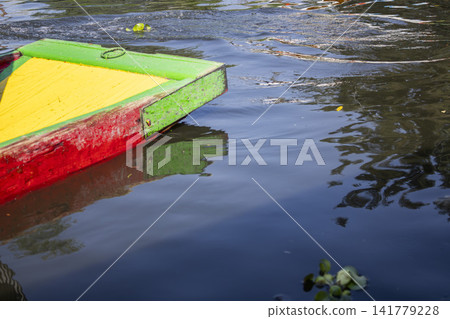 Xochimilco colorful wooden trajinera floating on calm water with reflections Xochimilco colorful wooden trajinera floating on calm water with reflections 141779228