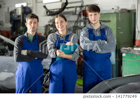 Team of auto mechanics, two men and one woman, wearing blue overalls and posing, ready to provide professional vehicle service Team of auto mechanics, two men and one woman, wearing blue overalls and posing, ready to provide professional vehicle service 141779249