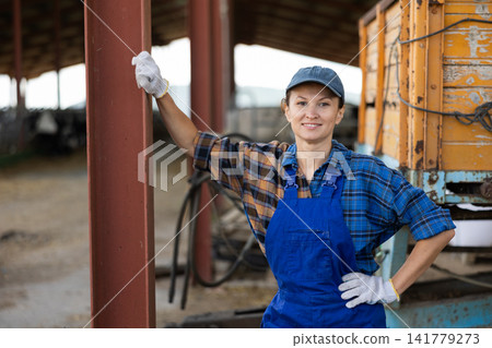 Portrait of woman in blue overalls in backyard of cowshed Portrait of woman in blue overalls in backyard of cowshed 141779273