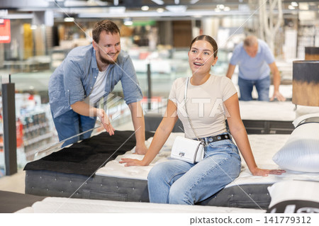 In furniture store, married couple examines orthopedic mattress. In furniture store, married couple examines orthopedic mattress. 141779312