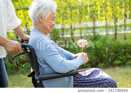 Asian senior or elderly old lady woman holding red rose flower, smile and happy in the sunny garden. 141780084