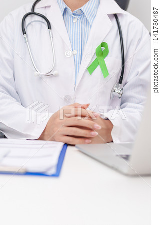 doctor using laptop and report notes on notebook. lime Green Ribbon for concept of May Celiac Awareness month, Lyme disease, September Lymphoma, Mental Health Awareness month and October Liver cancer doctor using laptop and report notes on notebook. lime Green Ribbon for concept of May Celiac Awareness month, Lyme disease, September Lymphoma, Mental Health Awareness month and October Liver cancer 141780487
