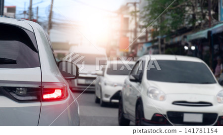 Cars turn on brake light and queued in heavy traffic congestion on a bright city street during the daytime commute. Cars on the opposite side were driving in a long line. With glaring sunlight. 141781154