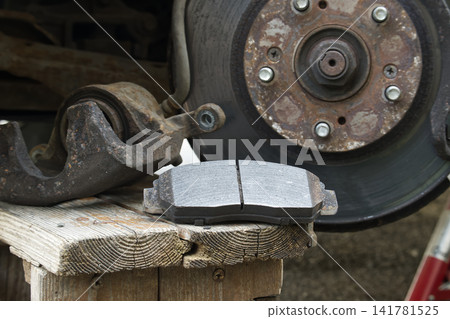 New brake pads resting on weathered wood next to a rusty car brake assembly New brake pads resting on weathered wood next to a rusty car brake assembly 141781525
