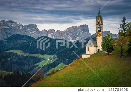 Small church with tall steeple on green hillside in mountains Small church with tall steeple on green hillside in mountains 141781608