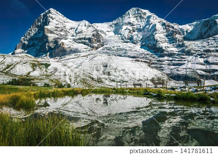 Snow-capped mountains with a calm lake and green grass Snow-capped mountains with a calm lake and green grass 141781611