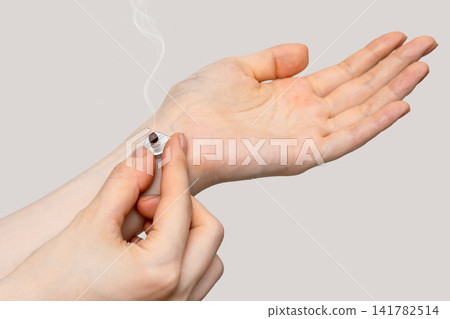 A woman's hand supporting a moxibustion treatment on the inside of her wrist with her fingers. A woman's hand supporting a moxibustion treatment on the inside of her wrist with her fingers. 141782514