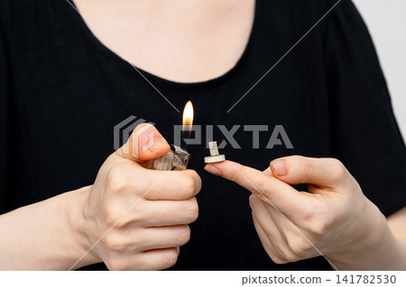 A woman brings a lighter flame close to the moxibustion base on her fingertip. A woman brings a lighter flame close to the moxibustion base on her fingertip. 141782530