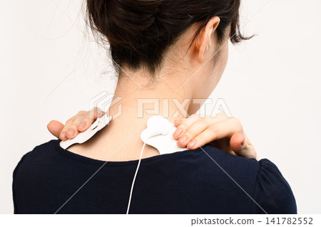 A woman's back view as she applies electrode pads to the area between her neck and shoulders. A woman's back view as she applies electrode pads to the area between her neck and shoulders. 141782552