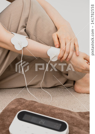 垂直拍攝的照片,顯示了手臂上的電極片和低頻治療設備。 垂直拍攝的照片,顯示了手臂上的電極片和低頻治療設備。 141782558