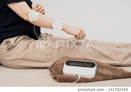 一名女子將低頻治療儀的電極片貼在手臂上。 一名女子將低頻治療儀的電極片貼在手臂上。 141782568