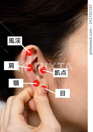 A woman pinching the acupressure points on her ears with her fingers. A woman pinching the acupressure points on her ears with her fingers. 141782587