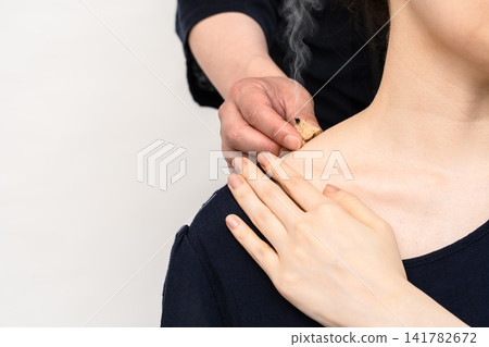 The hands adjusting the moxa moxibustion at the base of a woman's neck with their fingertips. The hands adjusting the moxa moxibustion at the base of a woman's neck with their fingertips. 141782672