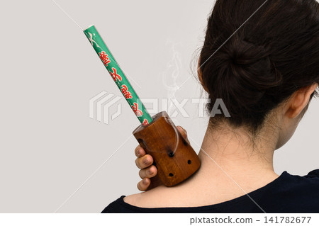 A woman's back as she brings a smoky moxa stick close to the nape of her neck. A woman's back as she brings a smoky moxa stick close to the nape of her neck. 141782677