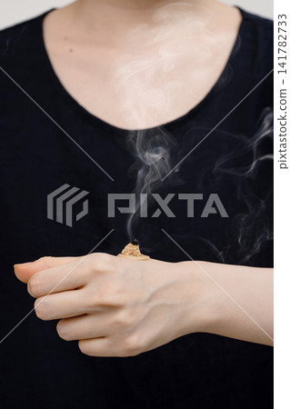 A woman's upper body as she lights the moxa for ginger moxibustion with an incense stick. 141782733