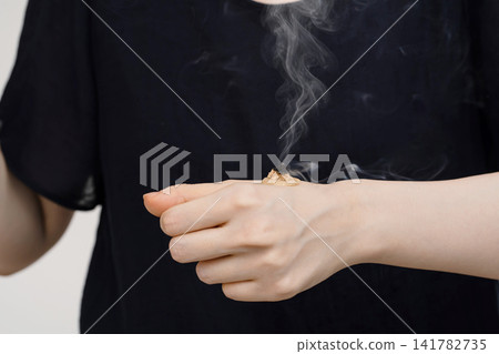 Ginger moxibustion burning and emitting smoke on the back of a woman's hand. 141782735