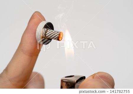 The hand holding the moxa cone with its base and lighting it with a lighter. The hand holding the moxa cone with its base and lighting it with a lighter. 141782755