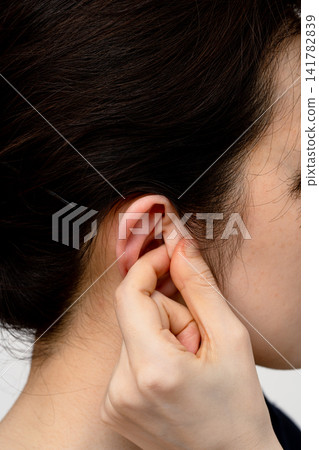 A woman pinches and stimulates the center of her ear with her fingers. A woman pinches and stimulates the center of her ear with her fingers. 141782839