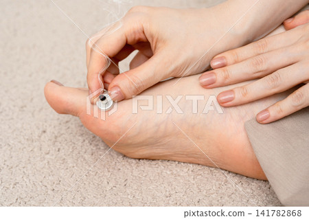 A woman's hands and beige clothing as she adjusts a moxibustion treatment on her ankle. A woman's hands and beige clothing as she adjusts a moxibustion treatment on her ankle. 141782868