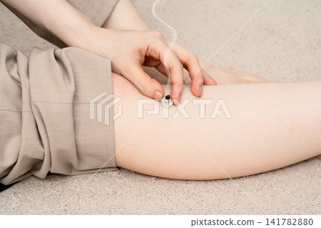 一名女子將手放在正在冒煙的桌上型艾灸器上,艾灸器正對著她的小腿。 一名女子將手放在正在冒煙的桌上型艾灸器上,艾灸器正對著她的小腿。 141782880