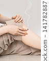 Smoke rises from a moxa cone near the knee of a woman's hands and legs. 141782887