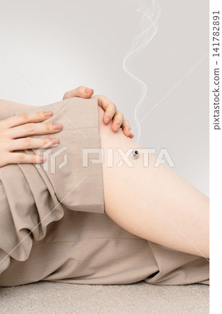 A woman's bent knees are used to place a smoky moxibustion device on a base, with both hands supporting it. A woman's bent knees are used to place a smoky moxibustion device on a base, with both hands supporting it. 141782891