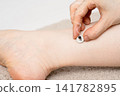 A hand supporting a moxa cone that emits smoke on a woman's ankle. 141782895