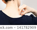A woman's back view as she places her hand on a moxa cone at the base of her neck. 141782909