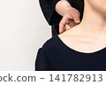 A woman places her hand on a cone-shaped moxa patch at the junction of her neck and shoulder. 141782913