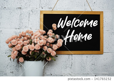 Welcome Home text on blackboard hanging on concrete wall and flowers in metal vase decoration Welcome Home text on blackboard hanging on concrete wall and flowers in metal vase decoration 141783232