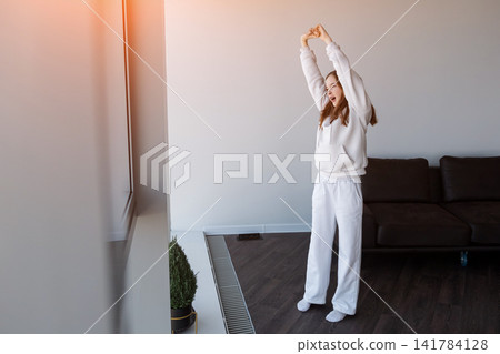 Young woman waking up, stretching in sunny morning room Young woman waking up, stretching in sunny morning room 141784128