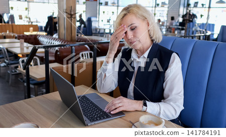 Stressful Female Professional Working. An Overwhelmed Senior Businesswoman Facing Deadlines At Busy Cafe. Distressed Professional Woman Struggles With Tasks Amidst Hurried Coffee Shop Environment Stressful Female Professional Working. An Overwhelmed Senior Businesswoman Facing Deadlines At Busy Cafe. Distressed Professional Woman Struggles With Tasks Amidst Hurried Coffee Shop Environment 141784191
