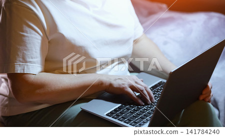 Woman hands working on a laptop computer at home during nighttime, typing on the keyboard while sitting on a bed, focusing on remote work or freelancing activities Woman hands working on a laptop computer at home during nighttime, typing on the keyboard while sitting on a bed, focusing on remote work or freelancing activities 141784240