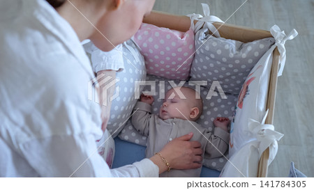 Young mother caring for sleeping newborn in crib Young mother caring for sleeping newborn in crib 141784305